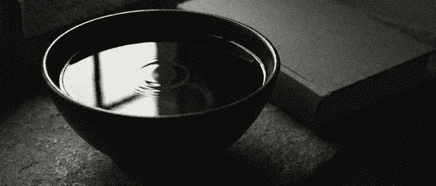 A black stoneware bowl brimming with water, a faint ripple ring on its surface, beside a closed grey book on a stone sill.