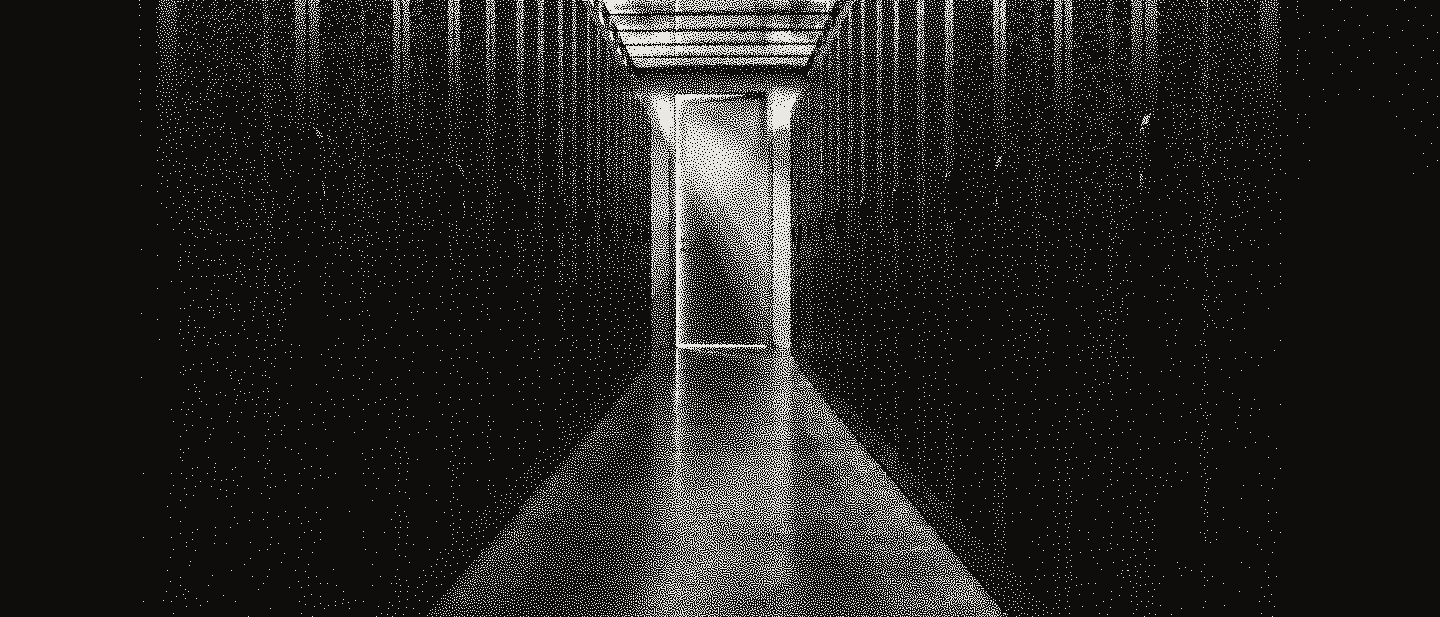 An empty corridor between rows of server racks, a lit open door at its far end.