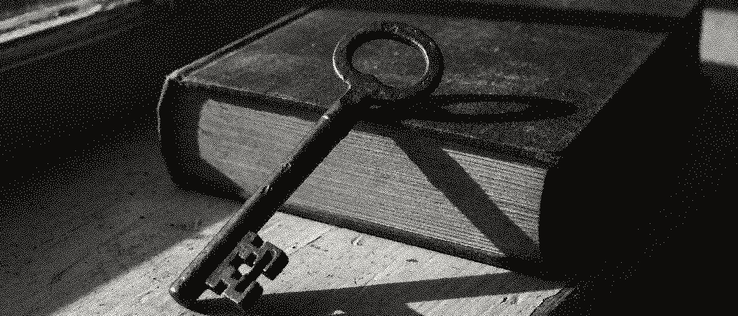 An old iron door key leaning against a closed red cloth book on a windowsill, in low evening sun.