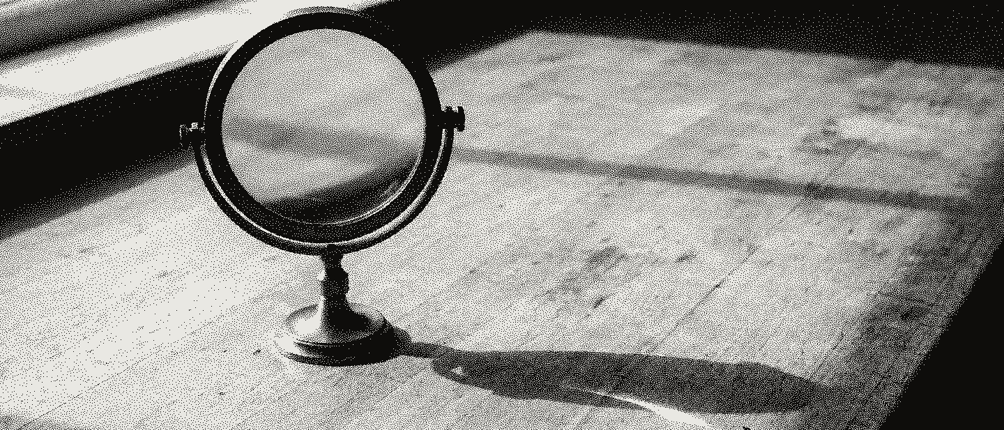 A magnifying lens in a brass ring on a stand, on a pale wooden lab bench in side light from a window.
