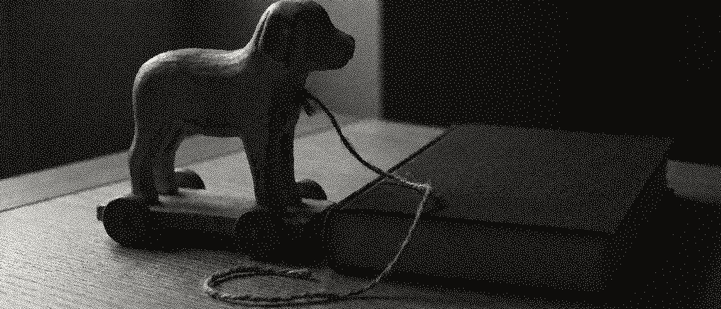 A worn wooden pull-along dog on wheels with a frayed string, beside a closed green cloth book on a light oak table.
