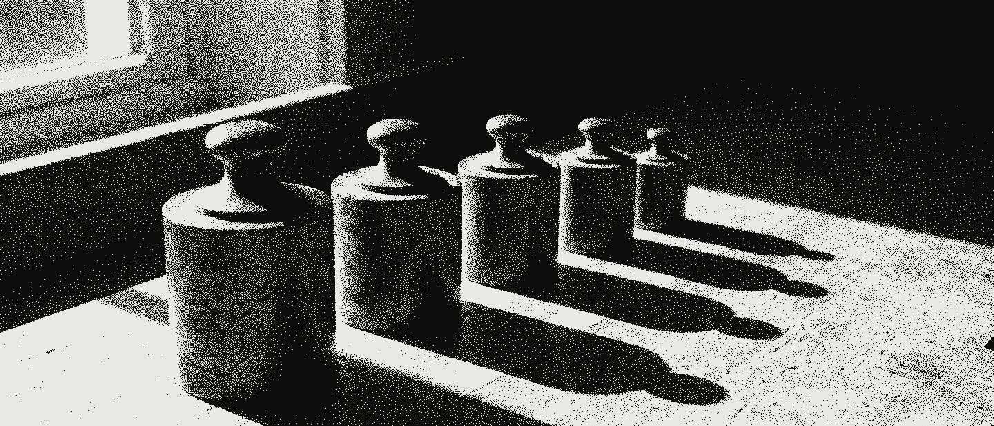 Five brass calibration weights with lifting knobs, standing in a row by size on a pale bench in hard sun.
